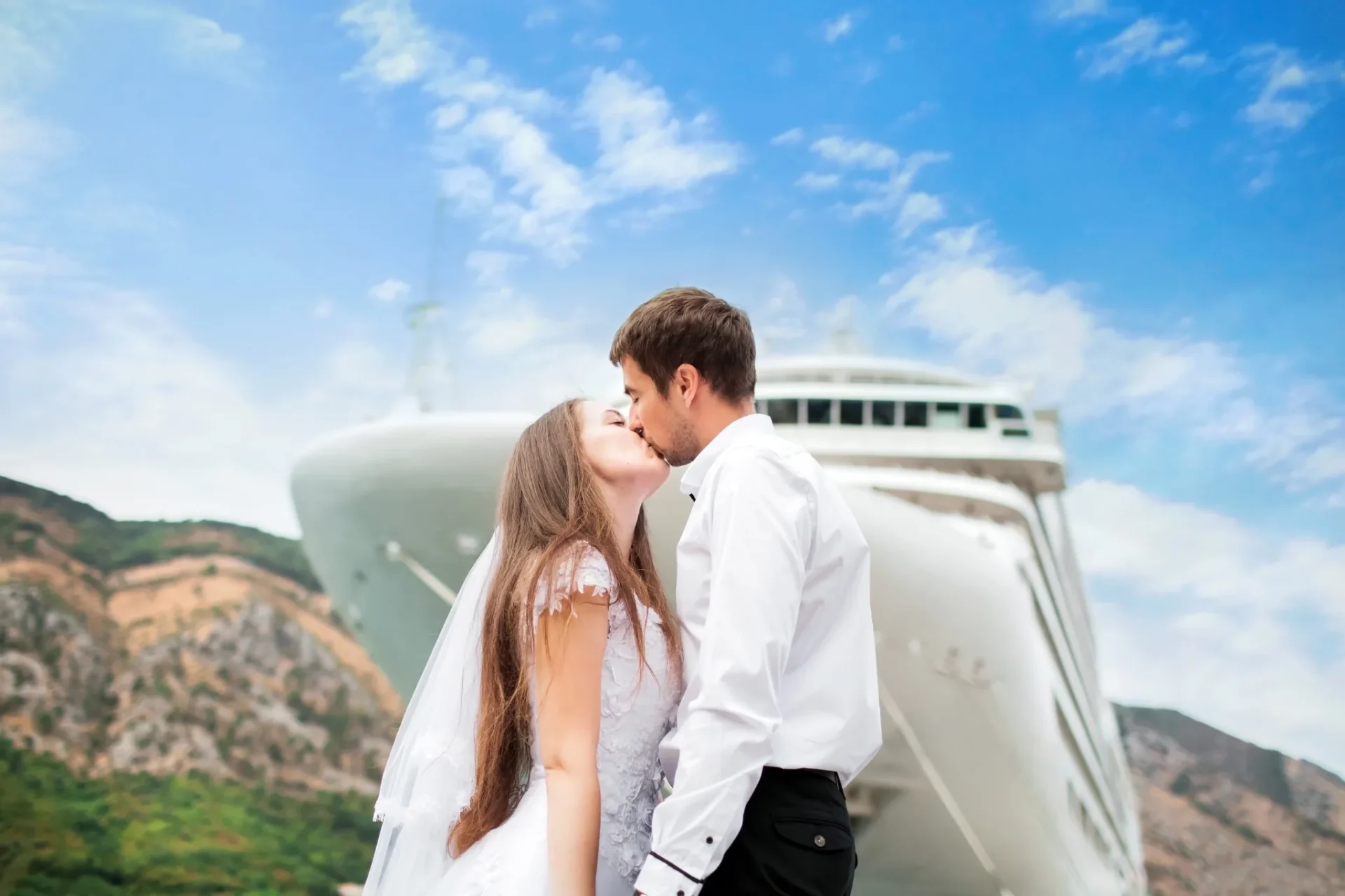 Bride and groom kissing in front of a cruise ship in St. Thomas with blue sky and island hills in the background.